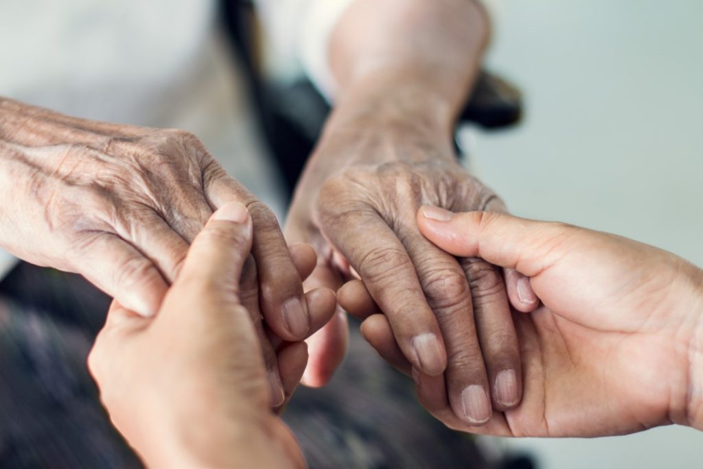 Mãos de cuidador de idoso pegando na mão de idoso