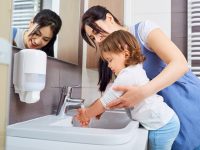 Kid washing hands with mom in the bathroom.