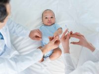 Bebê deitada em uma cama com os pais cuidando