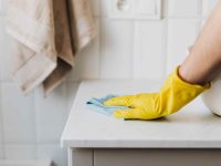 Mão usando luva de faxineira limpando mesa
