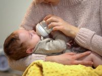 Babysitter feeding cute little child from bottle, artificial feeding accessories